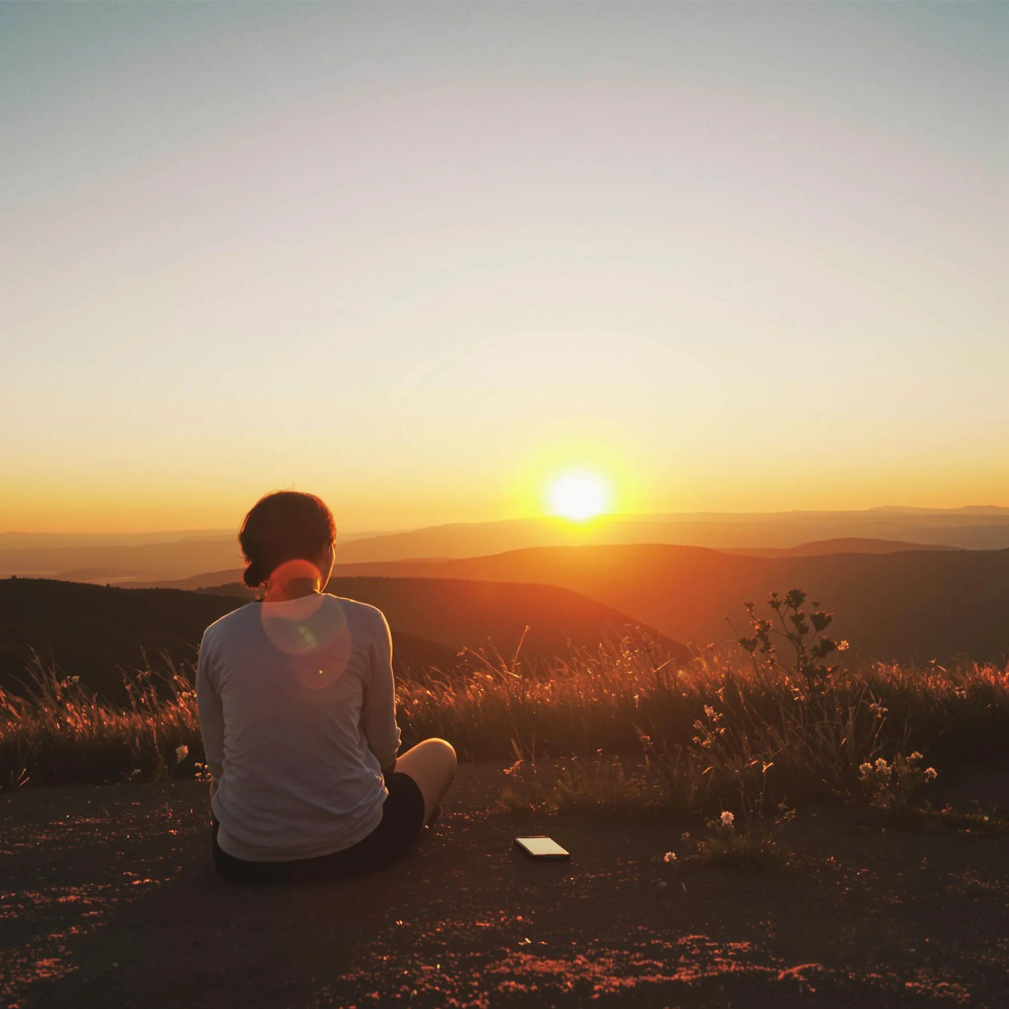 Peaceful person enjoying sunset on hilltop while smartphone lies ignored nearby.