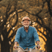An elderly man with gray hair riding a bicycle and looking straight ahead